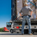 Trucker standing and looking at the rear of a trailer truck loaded with cargo.